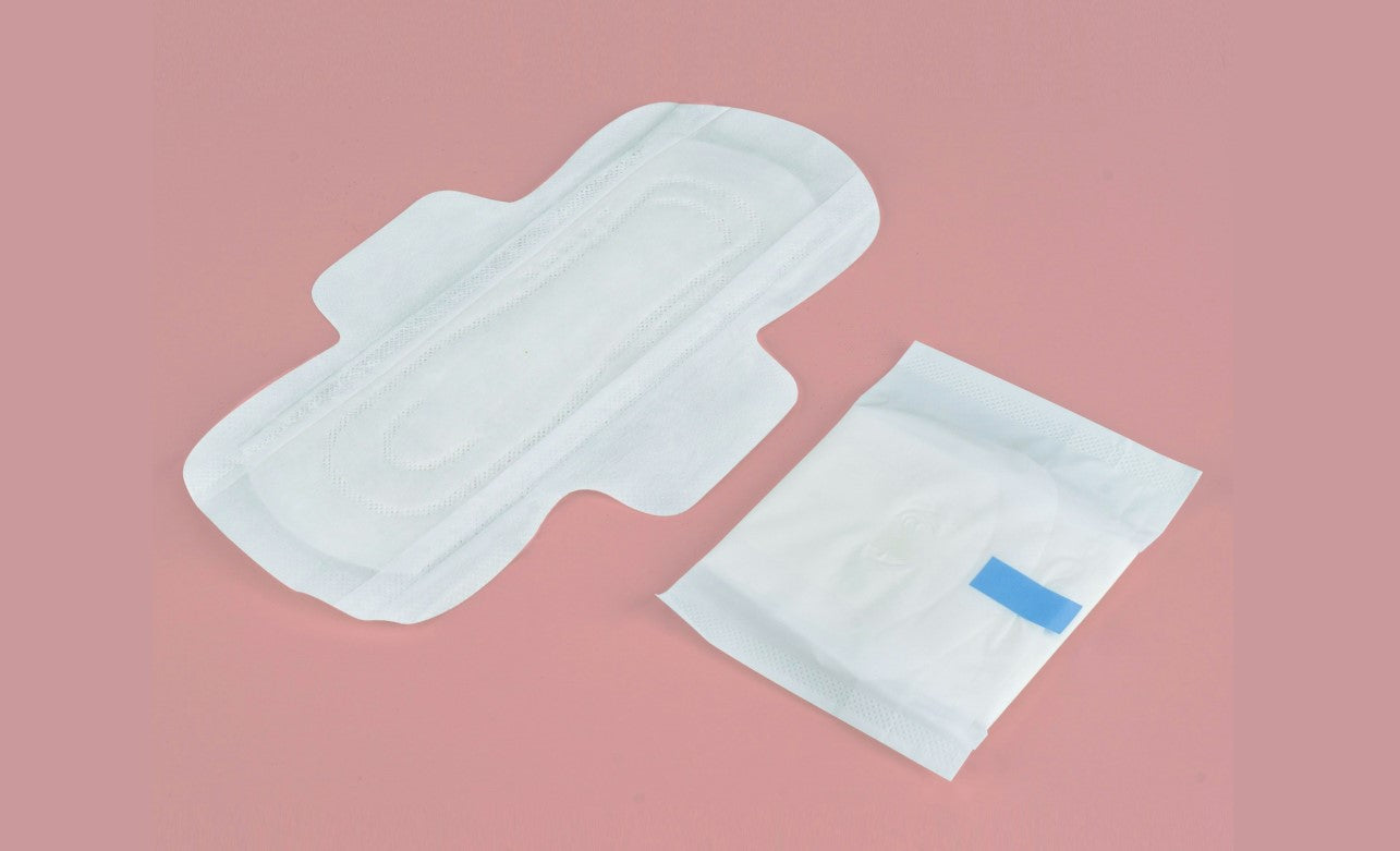Fizabelle pad ingredients: A sanitary pad lies next to its packaging on a pink background, highlighting feminine hygiene products.