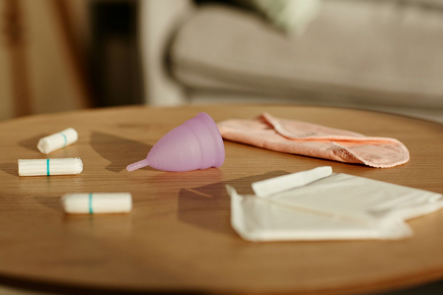 Period kit essentials: A purple menstrual cup sits on a wooden table alongside cotton tampons, a cloth pad, and sanitary napkins.