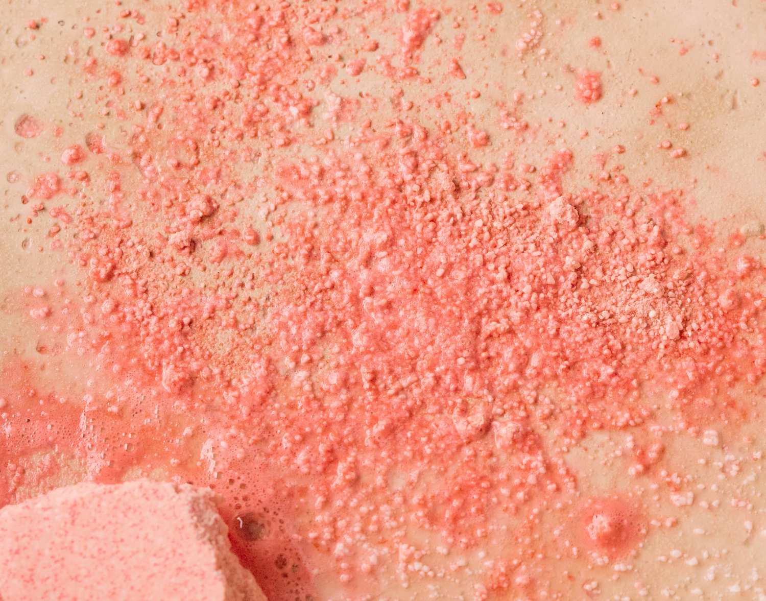 Close-up of pink bath powder scattered on a beige surface, with bubbles forming in areas, creating a rash-like texture, colorful display.