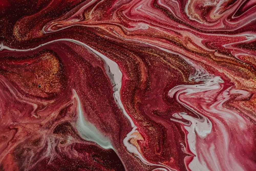 Menstrual flow changes by age: Abstract swirls of red, white, and gold create a vibrant, fluid pattern reminiscent of marble or flowing paint.
