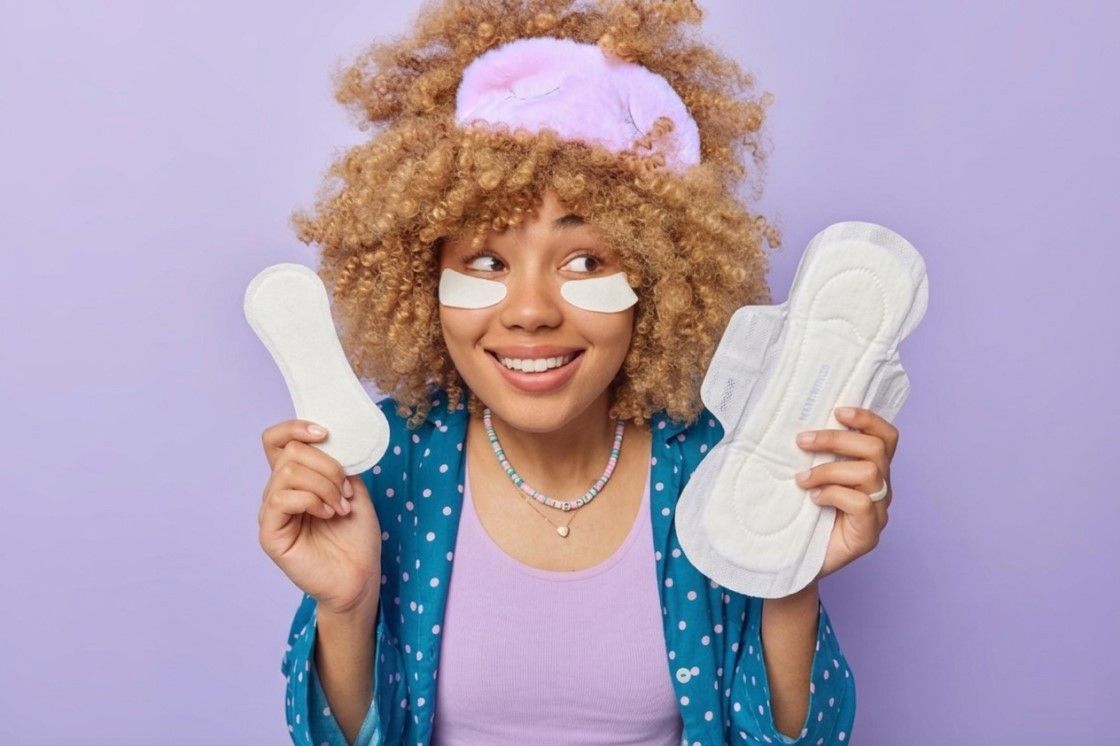 Three flow level pads: Person in polka dot robe and pink sleep mask holds two different sizes of sanitary pads against a purple background.